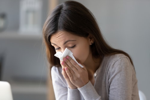 brunette female with allergies sneezing into a tissue